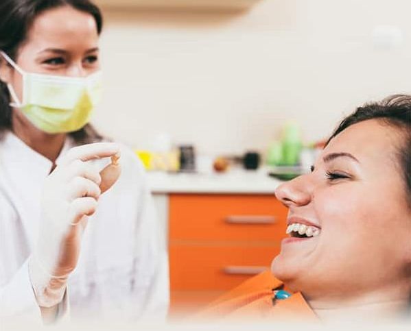 A dentist is holding an extracted tooth after a tooth extraction while a patient is in the dental chair smiling.